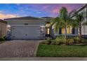 Charming single-story home features a well-manicured lawn, stone accents, and a brick driveway at dusk at 32773 Tree Of Life Ave, Wesley Chapel, FL 33543