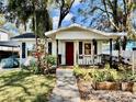 Charming single-story home featuring a covered porch, red door, and mature landscaping at 1210 E Sligh Ave, Tampa, FL 33604