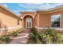 Elegant home entrance featuring an arched entryway, brick path, double doors, and manicured landscaping at 5062 Stone Harbor Cir, Wimauma, FL 33598