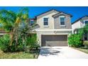 Two-story home with a neutral color scheme, well-kept lawn, two car garage, and tropical landscaping at 14430 English Lavender Dr, Wimauma, FL 33598