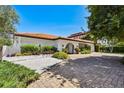 Inviting home with a white exterior, brick driveway, arched entryway, and mature landscaping at 205 Harrison Ave, Belleair Beach, FL 33786