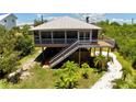 Charming stilt home with an outdoor deck and staircase surrounded by lush green landscaping at 9444 Rum Runner Road, Placida, FL 33946