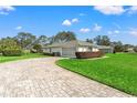 Exterior view of home showcasing a brick driveway, lush lawn, and mature trees at 9665 Southern Belle Dr, Weeki Wachee, FL 34613