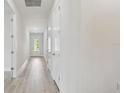 Bright hallway with light wood flooring and white walls, leading to a sunlit entryway at 11885 Richmond Trl, Parrish, FL 34219