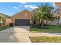 This house is painted tan and features a black two-car garage and manicured lawn at 11720 Winterset Cove Dr, Riverview, FL 33579