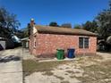 Quaint red brick home with chimney, side yard, and trash receptacles under a clear blue sky at 1609 W Knollwood St, Tampa, FL 33604