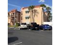 Exterior shot of a condo building with a peach facade, red roof, palm trees, and parked cars at 8901 Blind Pass Rd # 224, St Pete Beach, FL 33706