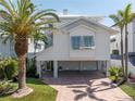 Charming stilt home with light-colored siding, garage, and inviting driveway lined with tropical palm trees at 8505 Blind Pass Dr, Treasure Island, FL 33706