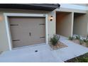 Attached garage featuring tan door with updated black iron hardware and manicured rock landscaping at 11115 Wishing Cloud Rd, Land O Lakes, FL 34638