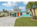 Charming exterior view of a one-story home showcasing colorful accents, a paved driveway, and mature landscaping at 1868 Douglas Ave, Dunedin, FL 34698
