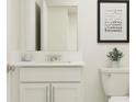 Modern bathroom featuring a white vanity, framed mirror, and toilet with contemporary art and plant at 5206 Meyer Bessie St, Zephyrhills, FL 33541