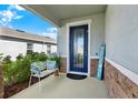 Welcoming front porch featuring a blue front door, bench with pillows, stone accents and lush greenery at 10432 High Noon Trl, Parrish, FL 34219