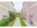 Exterior side yard of a pink townhome with landscaping and a pathway leading to a shared green space at 10011 Tranquility Way, Tampa, FL 33625