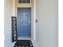 Stylish blue front door with a 'Welcome to Our Home' doormat on a stucco facade at 23958 Terracina Ct, Land O Lakes, FL 34639