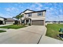 View of the two-story house showcasing the driveway, brown garage, green lawn, and landscaping at 13006 Tidal Flats Loop, Riverview, FL 33579