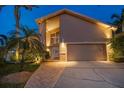 Well-lit home exterior with a two-car garage, a brick-paved walkway, and beautiful landscaping at twilight at 447 22Nd St, Belleair Beach, FL 33786