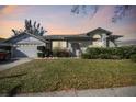 Charming single-story home with an attached two-car garage and well-manicured landscaping at sunset at 915 Brittany Park Blvd, Tarpon Springs, FL 34689