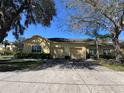 Beautiful tan home featuring an attached two-car garage, mature trees, and a paved driveway at 6359 Timberly Ln, Zephyrhills, FL 33542