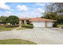 A home with a wide driveway, a three car garage, and a tile roof surrounded by lush landscaping at 30 Stanton Cir, Oldsmar, FL 34677