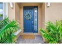 Blue front door with a wreath, a welcome mat, brick pavers, and lush tropical foliage at 10446 Highland Park Pl, Palmetto, FL 34221