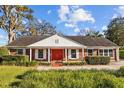 Charming brick home featuring a bright red front door, white trim, and a well-maintained front lawn at 14103 Lake Magdalene Blvd, Tampa, FL 33618