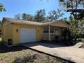 A cozy yellow home with a porch, attached garage, and mature landscaping in a sunny setting at 7111 N 53Rd St, Tampa, FL 33617
