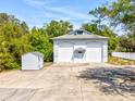 Light-blue home with white garage doors, gray roof, concrete driveway, and shed at 920 E Lake Dr, Tarpon Springs, FL 34688