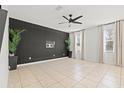 Bright living room with sleek black accent wall, tile flooring, ceiling fan and two large sunny windows at 707 Fern Leaf Dr, Ruskin, FL 33570
