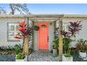 Inviting front porch with a bright coral door, stone walkway, and lush tropical plants at 6202 Tennessee Ave, New Port Richey, FL 34653
