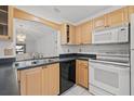 A bright kitchen with wood cabinets, black countertops, and white appliances with white tile flooring at 725 83Rd N Ave # 205, St Petersburg, FL 33702