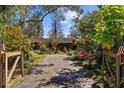 Lovely home viewed from gated driveway showcasing mature trees and lush, colorful landscaping at 17119 Rainbow Ter, Odessa, FL 33556