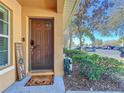 Welcoming brown front door with decorative welcome sign and mat situated beside a tidy landscaped yard and parking area at 9873 Trumpet Vine Loop, Trinity, FL 34655