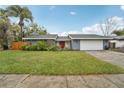 Single-story home featuring a manicured lawn, grey exterior, red door, and a two-car garage at 15639 Bear Creek Dr, Tampa, FL 33624