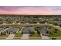 Aerial view of a residential neighborhood showcasing well-maintained homes with manicured lawns against a colorful sunset backdrop at 12749 Weatherstone Dr, Spring Hill, FL 34609