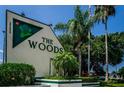 Entrance sign for 'The Woods' community featuring lush greenery and palm trees under a clear blue sky at 39650 Us Highway 19 N # 1422, Tarpon Springs, FL 34689