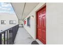 Exterior view of a condo's walkway featuring a red door and balcony with black railings and building facade at 11706 Raintree Village Blvd # D, Temple Terrace, FL 33617