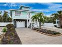 Stunning two-story coastal home with single garage, stairs to the balcony, stone accents, palm trees, and brick-lined flower bed at 311 Poinsettia Rd, Anna Maria, FL 34216