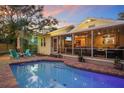 Beautiful backyard with a sparkling pool, brick patio, outdoor seating, and lush landscaping at twilight at 235 Aberdeen St, Dunedin, FL 34698