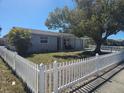 Street view of a home with a well-kept lawn, mature tree, and white picket fence at 3136 Primrose Dr, Holiday, FL 34691