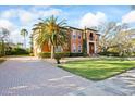 Elegant two-story home boasts a terracotta exterior, mature palms, a brick driveway, and manicured lawn at 5910 La Rosa Ln, Apollo Beach, FL 33572