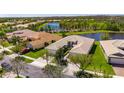 Aerial view of beige single Gathering home with red roof tiles next to a lake surrounded by trees at 15657 Aurora Lake Cir, Wimauma, FL 33598