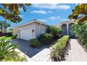 Beige single Gathering home with paver driveway, landscaping and front entrance portico with white columns at 15657 Aurora Lake Cir, Wimauma, FL 33598