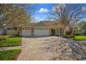 Long brick paver driveway leading to a three-car garage with mature landscaping and a manicured lawn at 17807 Crystal Cove Pl, Lutz, FL 33548