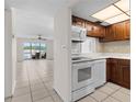 A view of the kitchen showcasing dark wood cabinetry, white appliances, and a breakfast bar leading to the living area with a balcony view at 1 Boca Ciega Point Blvd # 211, St Petersburg, FL 33708