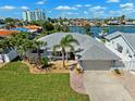 Waterfront home features mature landscaping, a gray roof, an attached garage, and a brick driveway at 6410 3Rd Palm Pt, St Pete Beach, FL 33706