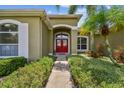 Inviting entrance of Florida home with a red double door, lush landscaping, and mature palms at 1403 Crooked Stick Dr, Valrico, FL 33596