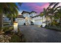 Beautiful two-story white home with a brick driveway and lush tropical landscaping at sunset at 3006 Christophers Watch Ln, Ruskin, FL 33570