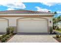 Exterior of home displaying two-car garage with paver driveway and minimal landscaping at 20411 Symphony Pl, Venice, FL 34293