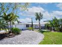 Charming single-story home featuring a brick driveway and beautifully manicured lawn with tropical trees at 218 Leeward Is, Clearwater Beach, FL 33767