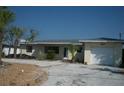 Charming single-story home with a light-colored exterior, garage, and a driveway, surrounded by lush greenery at 390 Belle Point Dr, St Pete Beach, FL 33706